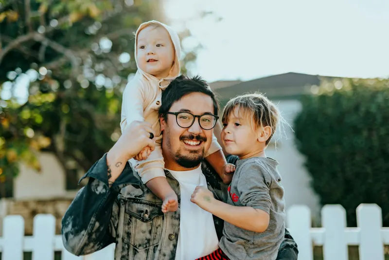 Father laughing while carrying his two young children
